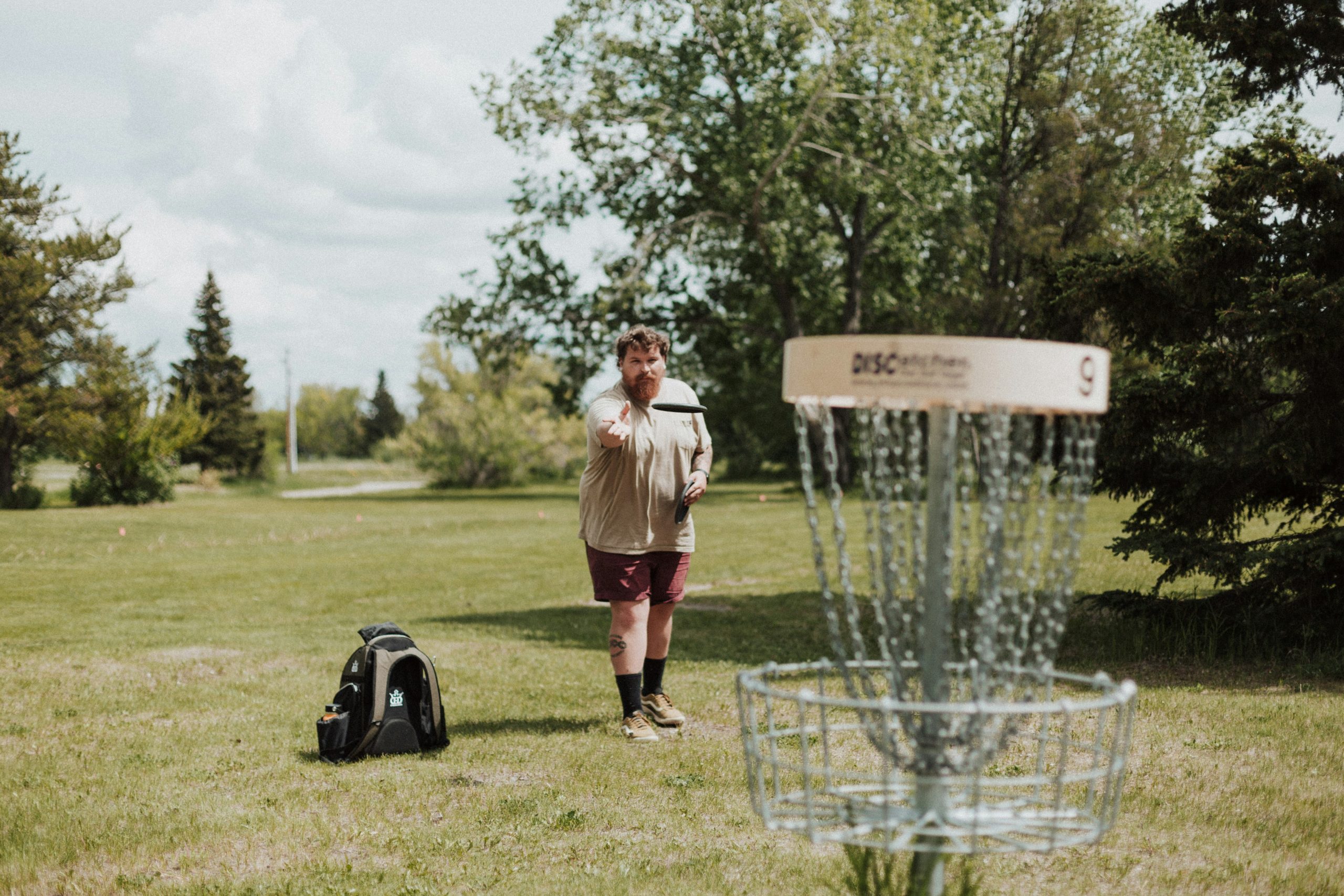 A man throwing a disc at a disc golf course basket target. A man throwing a disc at a disc golf course basket target.