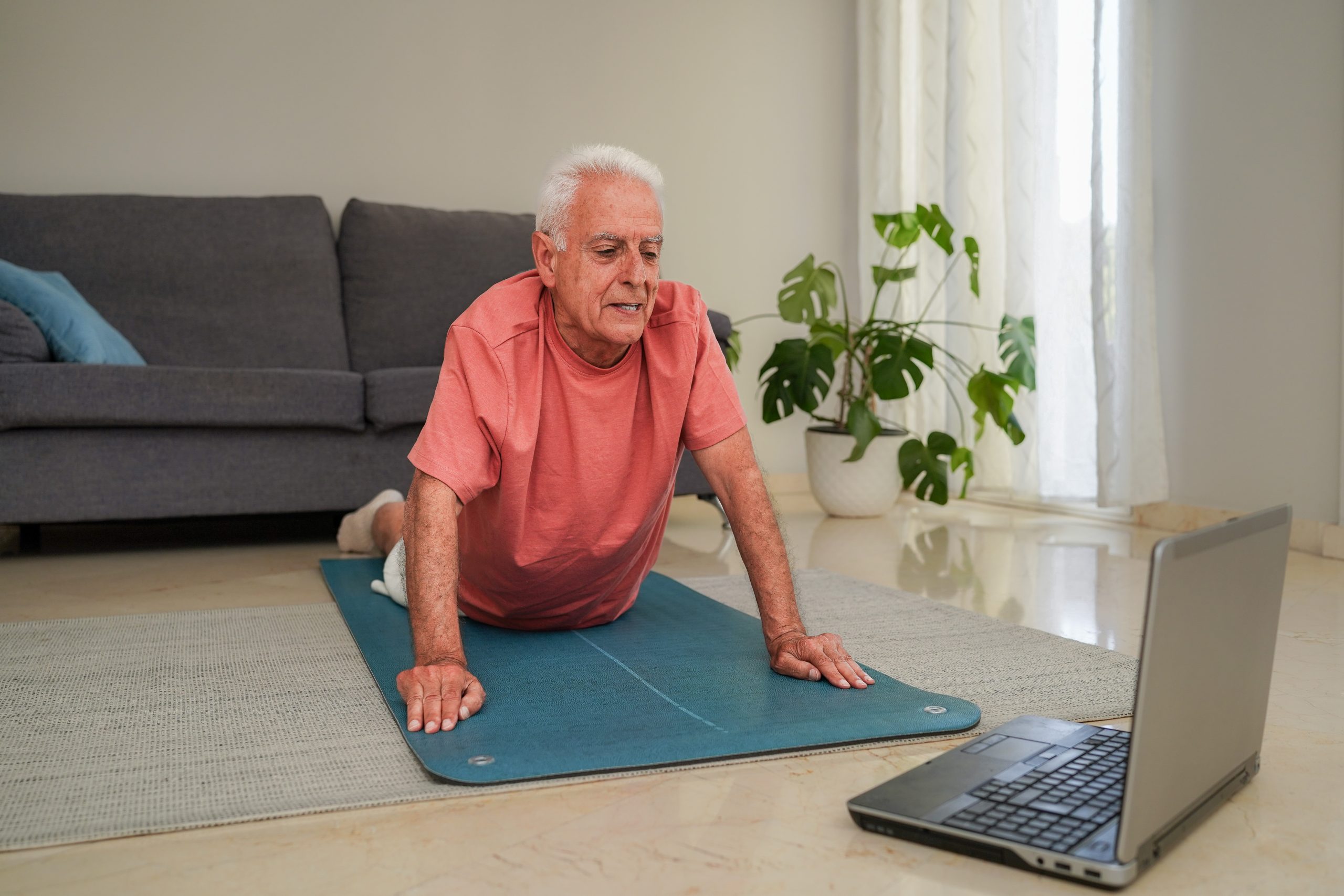 Un homme fait du yoga dans un salon devant un ordinateur portable. Un homme fait du yoga dans un salon devant un ordinateur portable.