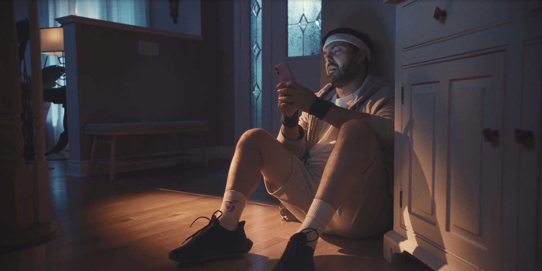 Un homme en tenue de sport assis sur le sol de l’entrée, regardant son téléphone intelligent. Un homme en tenue de sport assis sur le sol de l’entrée, regardant son téléphone intelligent.