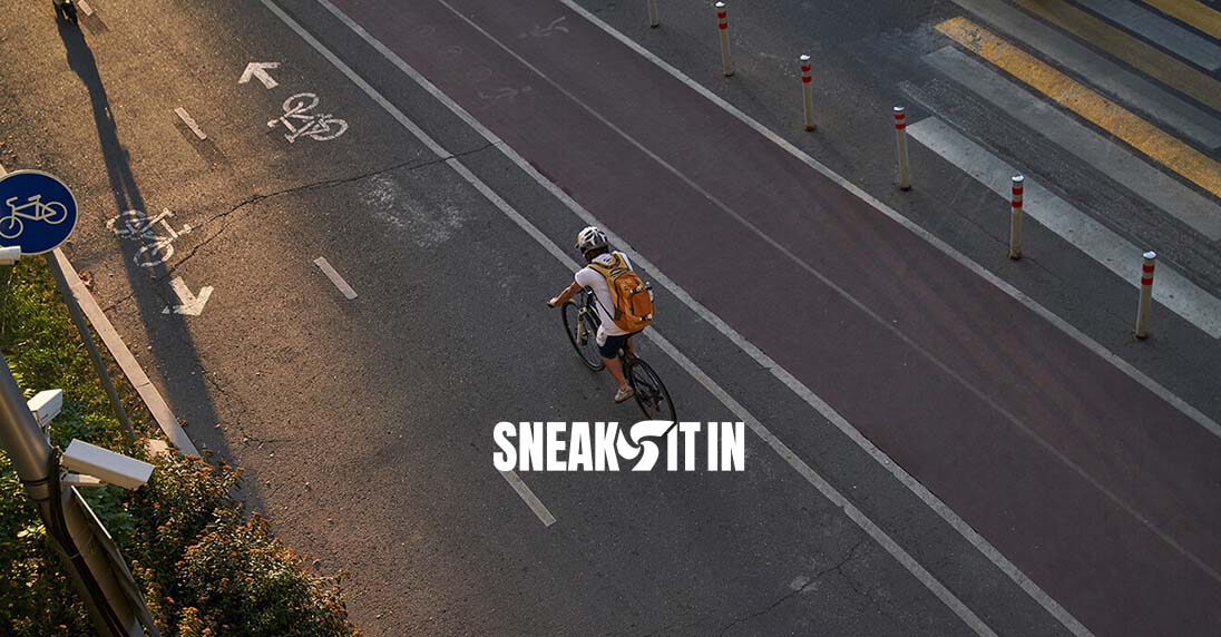 overhead view of a cyclist on the road with sneak it in and optimity logos overhead view of a cyclist on the road with sneak it in and optimity logos