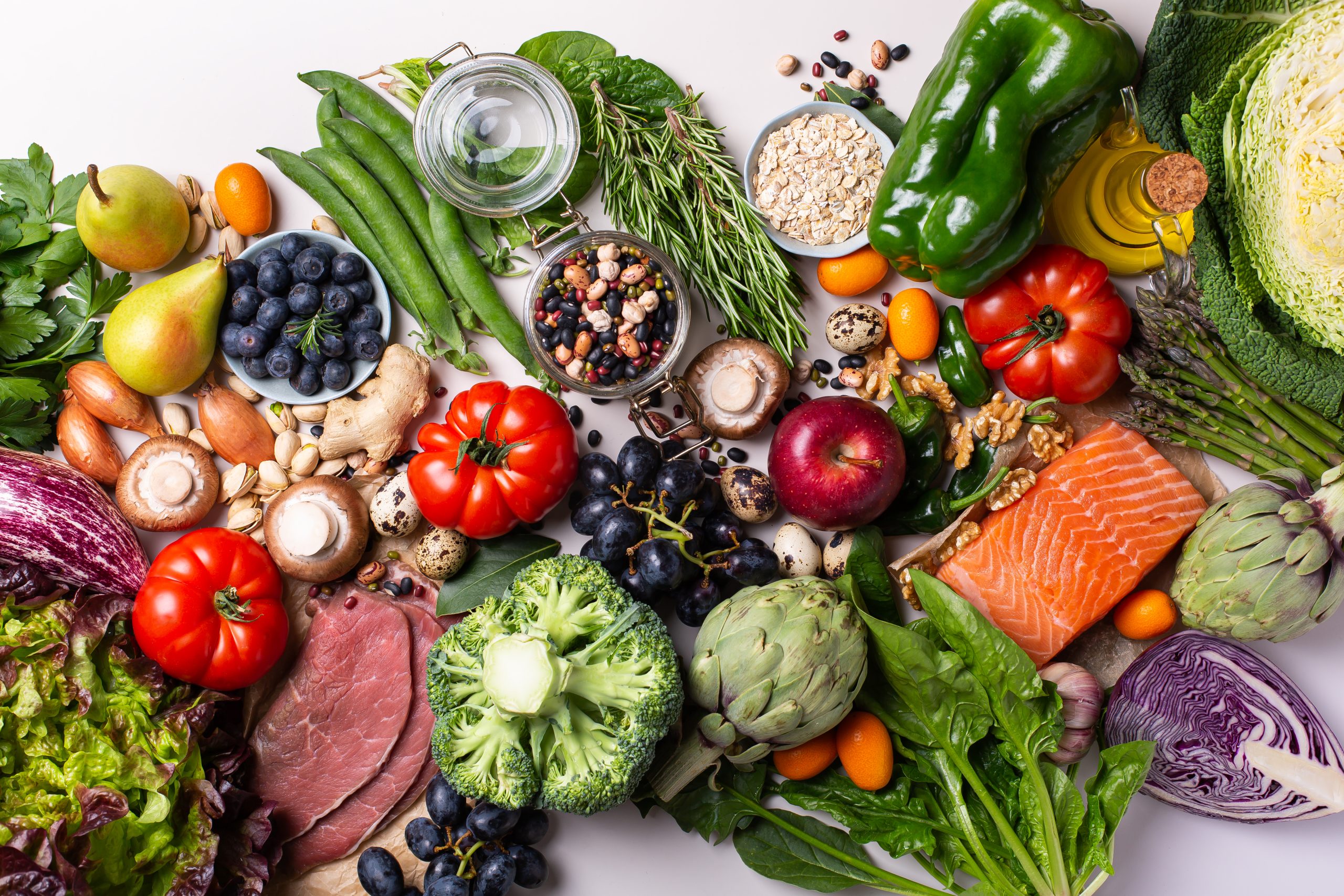 An assortment of vegetables, fruit, grains, salmon and cold cuts on a table. 