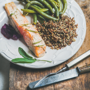 A plate with a salmon filet, green beans and quinoa.