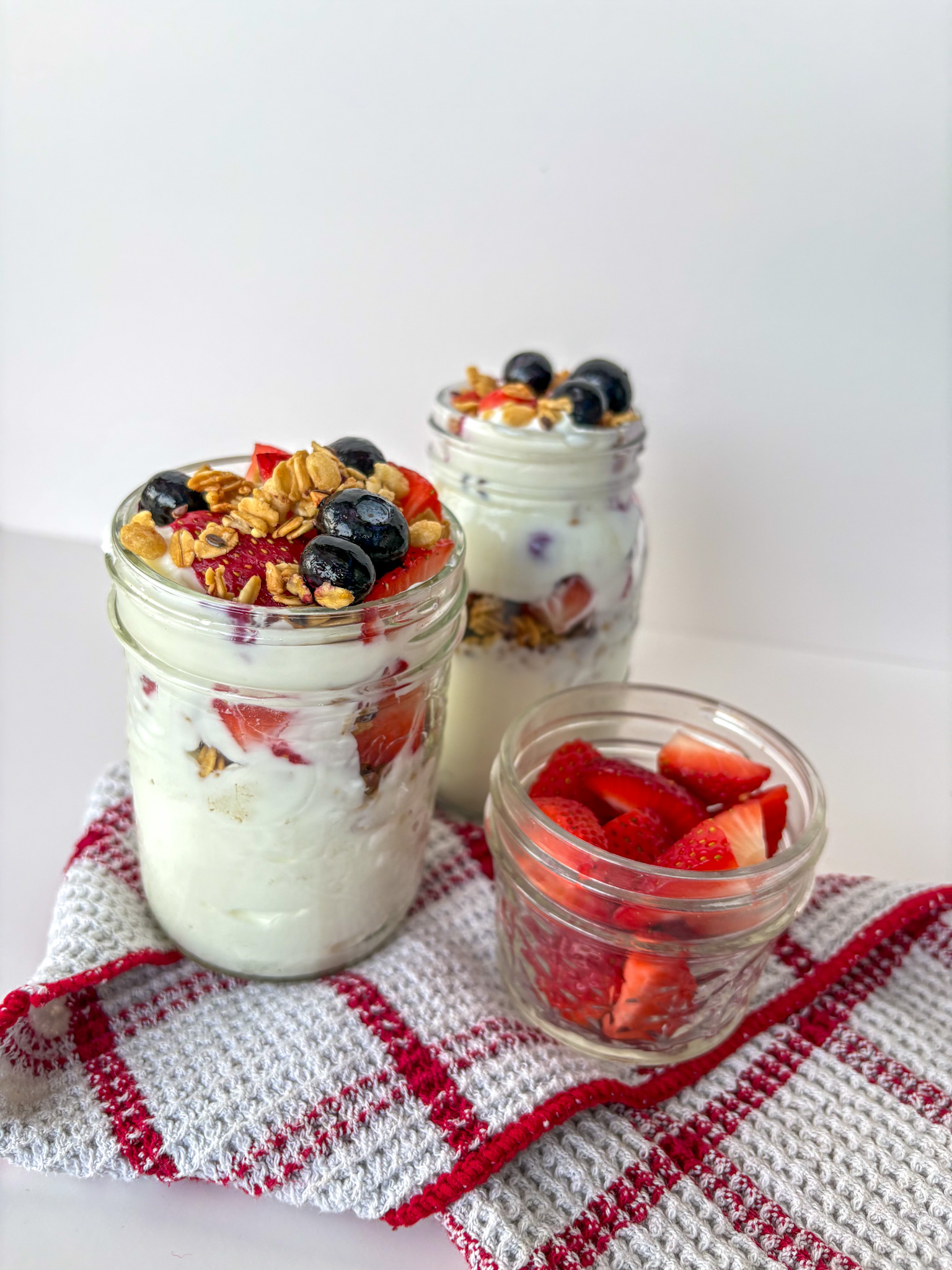 Berry and granola yogurt parfaits in jars on a table. Fuel your movement recipe of the month: Berry and granola yogurt parfait